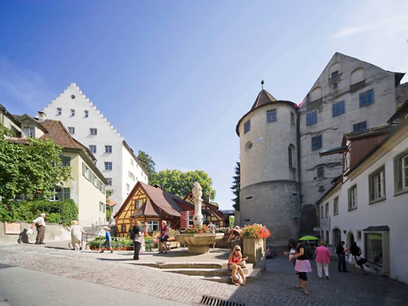 Platz in Hitweiler. Mehrere Menschen stehen und laufen vor den alten Gebäuden die im Hintergrund sind.