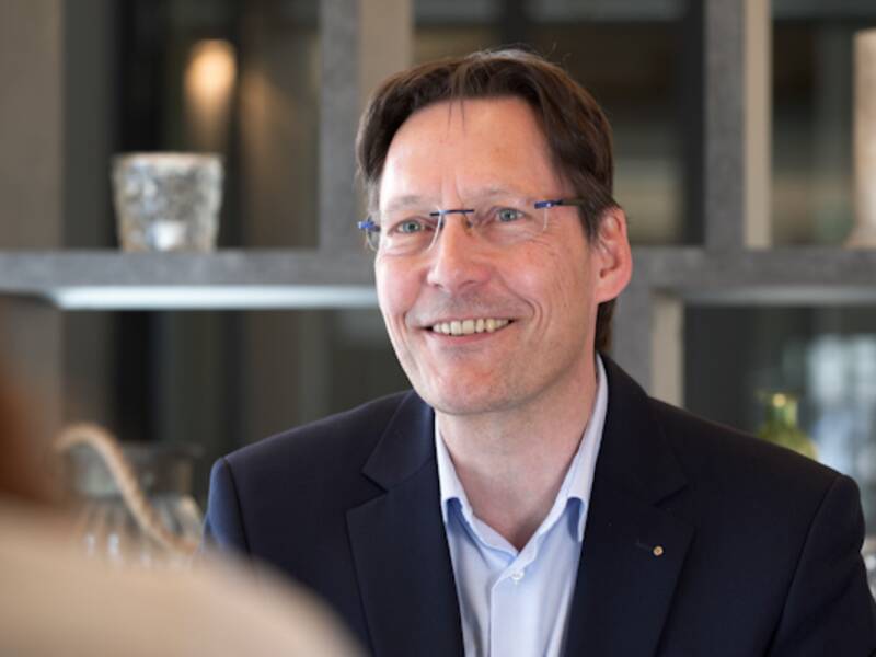 Portraitaufnahme eines Mannes mit kurzen Haaren und Brille. Er trägt ein hellblaues Hemd und ein dunkelblaues Sakko. 